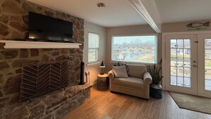 Ein Wohnzimmer mit Kamin aus Stein, einem Flachbildfernseher, einer gepolsterten Couch und einem großen Fenster mit Blick auf einen Park.