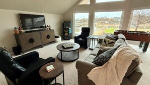 Ein Wohnzimmer mit Sofa, Sesseln, Couchtisch, Fernseher und Kicker.