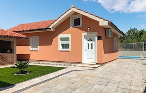 A two-story house with a red-tiled roof, a white door, and a small window.