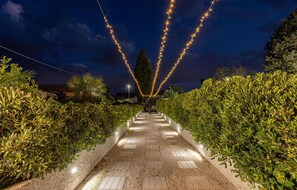 A pathway lined with greenery and illuminated by string lights, leading to a building in the distance. - Beautiful home in Chiaramonte Gulfi (Chiaramonte Gulfi)