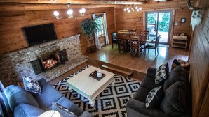 Interior acogedor de una cabaña con chimenea, paredes de madera, zona de comedor y sofá.