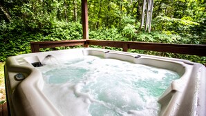 Un jacuzzi rodeado por una terraza de madera con vistas al bosque.