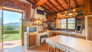 A kitchen with wooden cabinets, a gas stove, a microwave, and a large window overlooking a garden.