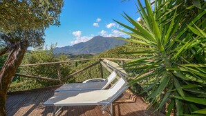 A wooden deck with a white lounge chair and a metal railing overlooking a mountainous landscape.