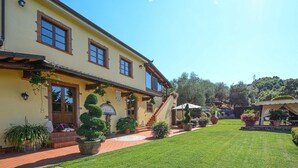 A two-story building with a yellow facade, multiple windows, and a well-maintained garden with potted plants and a lawn.