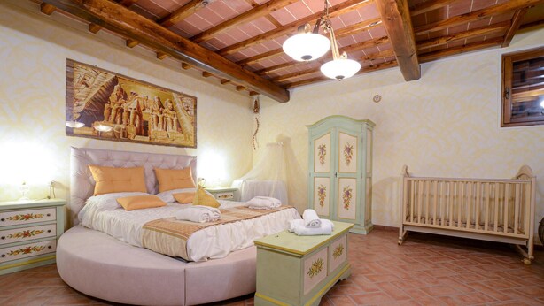 A bedroom with a round bed, a nightstand, a dresser, a crib, and a painting on the wall.