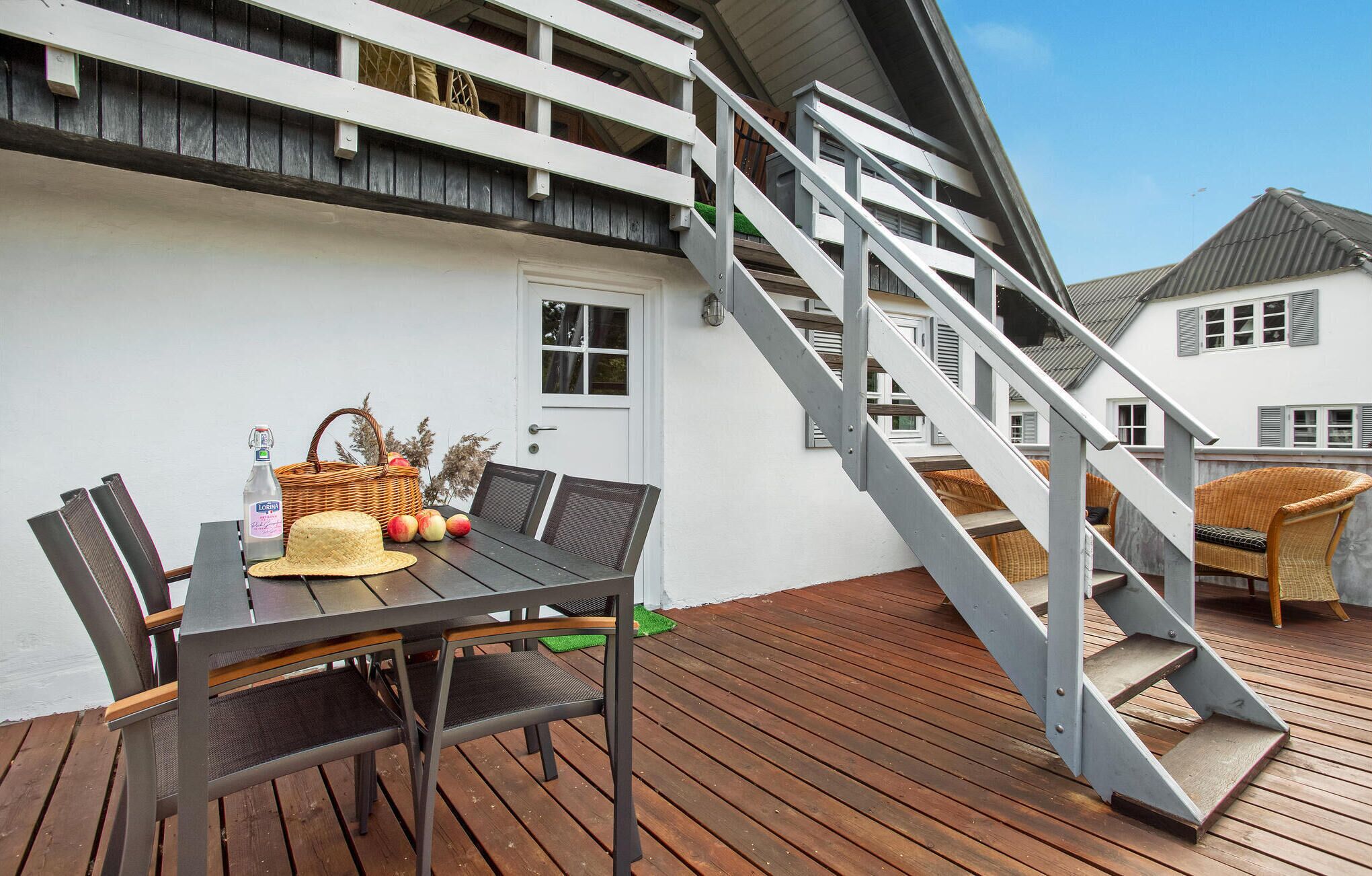 Eine Holzterrasse mit Esstisch, Stühlen und einem Korbwannen mit Äpfeln und einer Flasche.