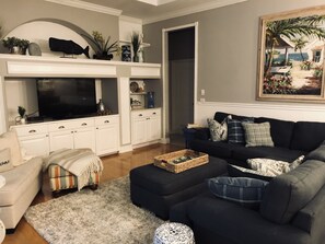 Un salon avec un téléviseur, des meubles blancs, un canapé noir et un tableau au mur.