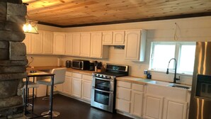 A modern kitchen with white cabinets, stainless steel appliances, a wooden ceiling, and a stone accent wall. - Quiet 2 story Cabin on 32 acres near eleven point river (Alton)