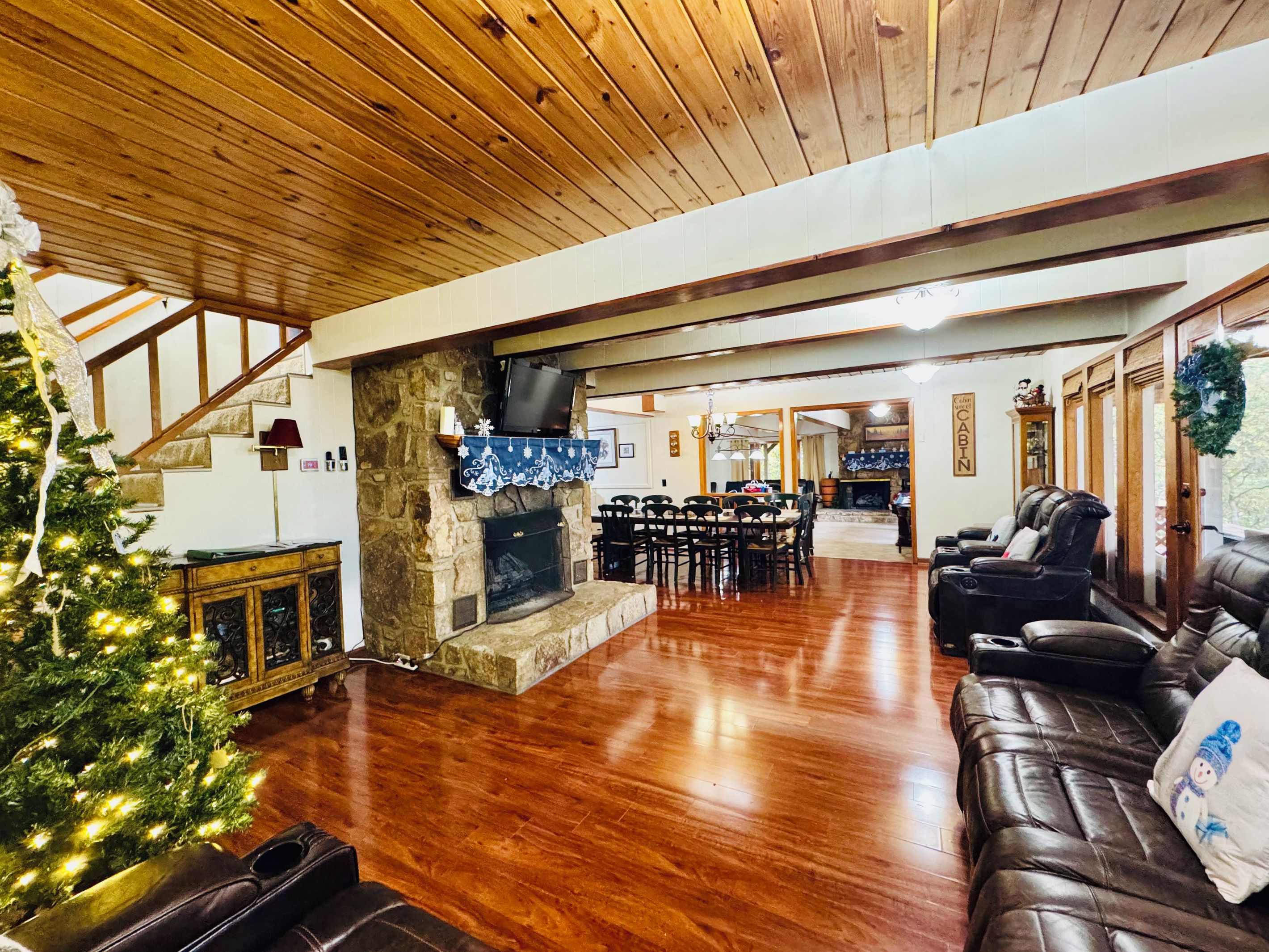 Un salón espacioso con chimenea de piedra, sofá de cuero y un árbol de Navidad.