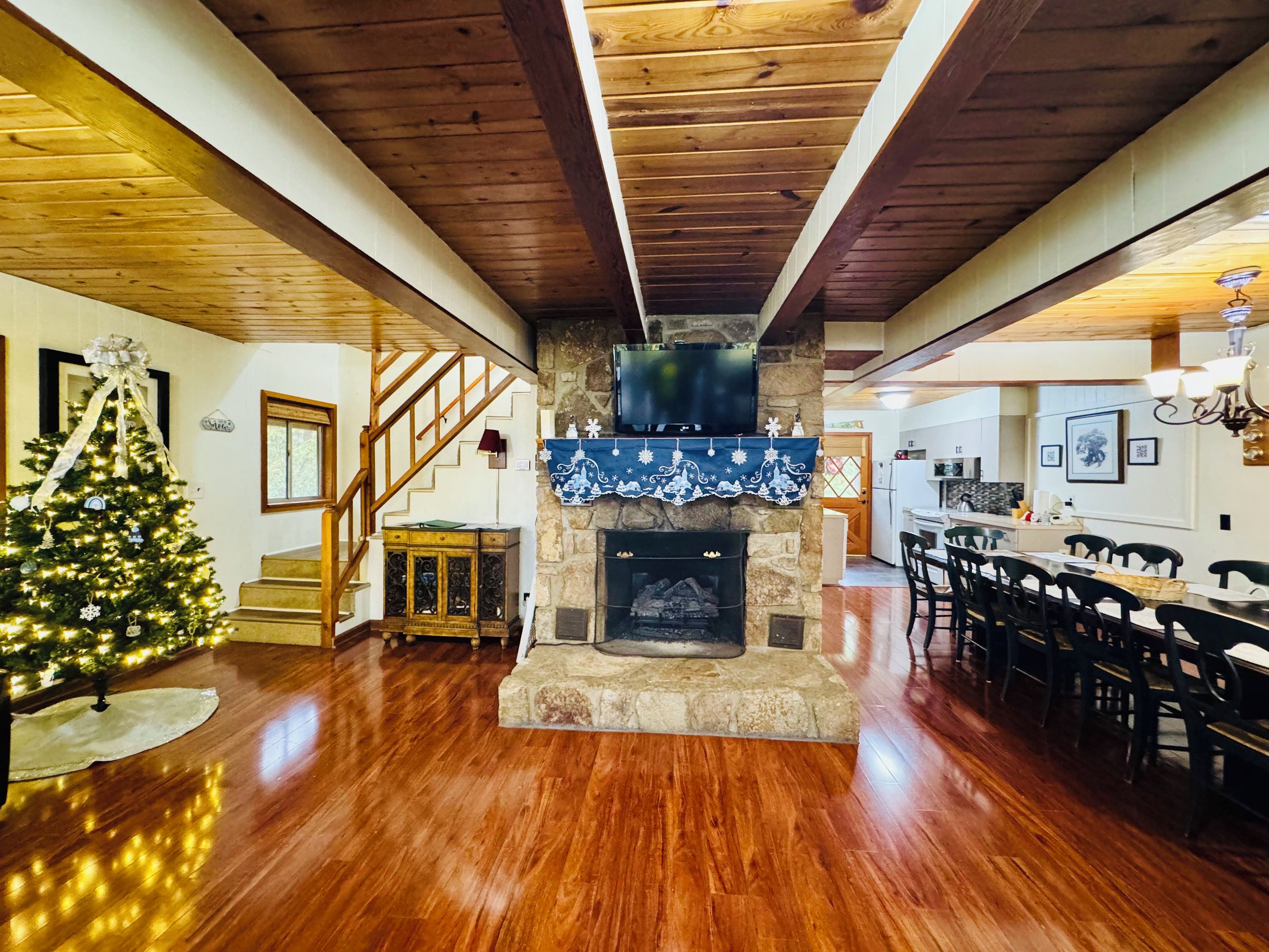 A spacious living room with a wooden floor, a fireplace, a Christmas tree, and a staircase.