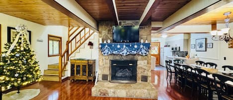A spacious living room with a wooden floor, a fireplace, a Christmas tree, and a staircase.