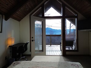 A room with a bed, a desk, and a view of mountains through a door.