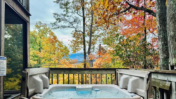 A hot tub on a wooden deck with a view of autumn trees.