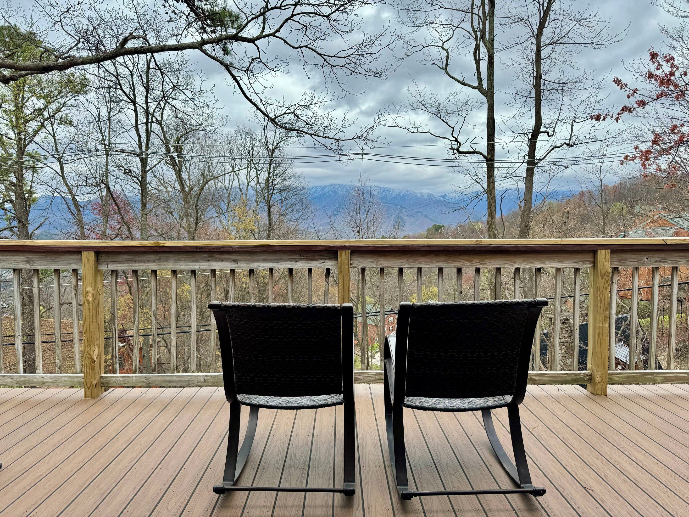 A wooden deck with two chairs facing a mountainous landscape.