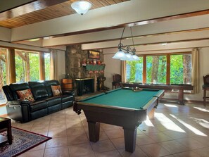 Une pièce spacieuse équipée d’une table de billard, d’un canapé en cuir, d’une cheminée et de grandes fenêtres.