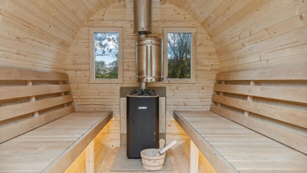 A sauna room with wooden walls, two windows, a central heating unit, and a wooden bench. - Awesome home in Nibe with kitchen (Nibe)