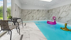 An indoor swimming pool with a view of greenery outside, a table with chairs, and a swan-shaped inflatable toy. - Awesome home in Nibe with kitchen (Nibe)