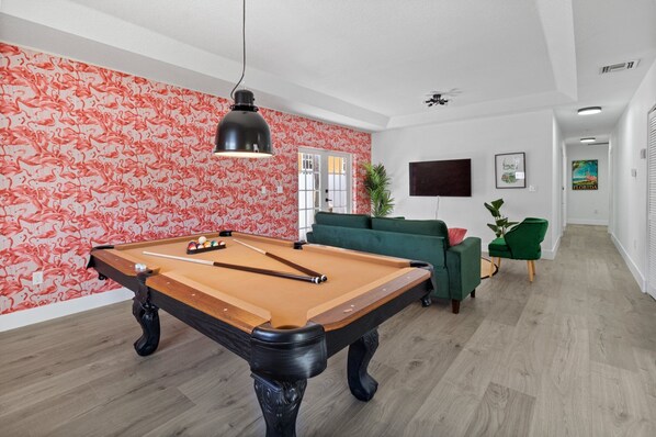 A pool table in a room with a red floral wallpaper, a green sofa, and a television on the wall.