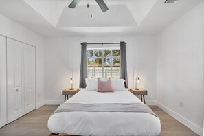 A bedroom with a large bed, a skylight, a window with curtains, and bedside lamps.