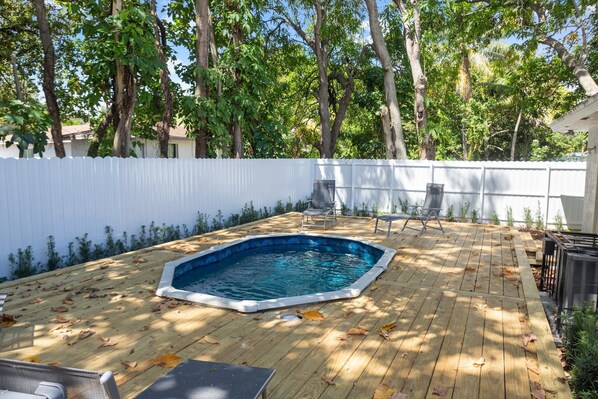 Un jardin avec une terrasse en bois, une piscine et deux chaises.