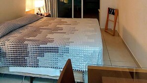 Une chambre d’hôtel équipée d’un lit, d’un bureau, d’une chaise, d’un téléviseur fixé au mur et d’une porte coulissante donnant sur un balcon.