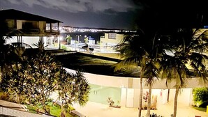 Vue nocturne d’une cour d’hôtel, avec des palmiers, une piscine et un bâtiment dont les fenêtres sont illuminées.