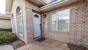 A brick house with a stone front porch, a white door, and a window with blinds. - Modern Smart Townhouse | Premium Amenities | Nearby Restaurants | Full Kitchen (El Paso)