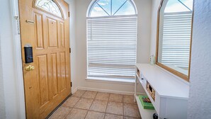 A hallway with a wooden door, a window with blinds, and a white counter with a mirror. - Modern Smart Townhouse | Premium Amenities | Nearby Restaurants | Full Kitchen (El Paso)