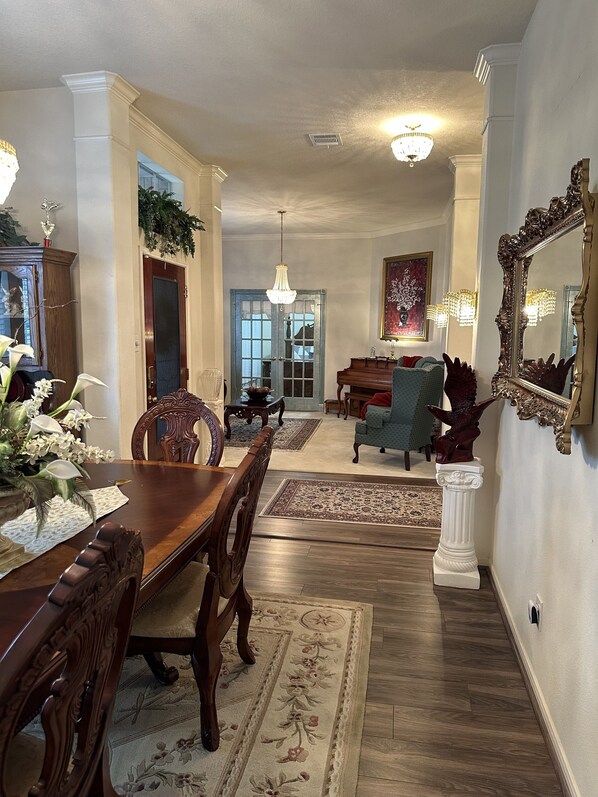 A dining room with a wooden table and chairs, a chandelier, and a large mirror on the wall.