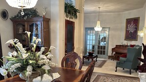 A dining room with a wooden table, chairs, and a chandelier. There is a piano and a green armchair in the background. - Unwind and Relax 4 Bedroom Stay (Humble)