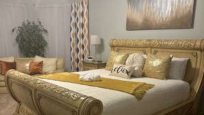A large ornate bed with a gold frame, a bedside table, a lamp, and a plant in a hotel room. - Unwind and Relax 4 Bedroom Stay (Humble)