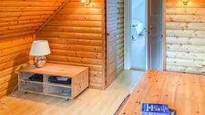 Una habitación acogedora de madera con una cama, una mesita con una lámpara y una puerta corredera que da a otra habitación.