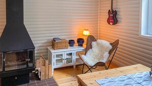 Un acogedor interior de cabaña con estufa de leña, una guitarra colgada en la pared y un sillón con un cojín mullido.