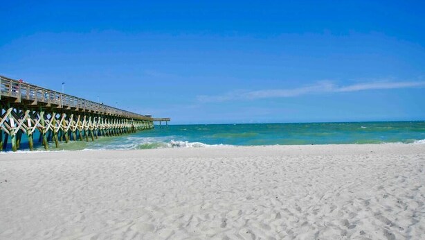 A beach with a wooden pier extending into the ocean.