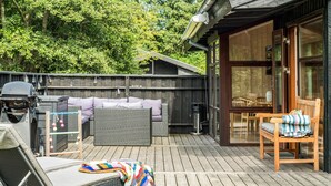 Una terraza con mobiliario exterior, una parrilla y una puerta de cristal que da a un espacio interior.