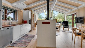 Una cocina moderna con estufa integrada, un comedor con televisor y grandes ventanas con vistas al exterior.