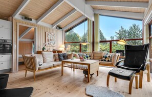 A spacious living area with a high ceiling, wooden beams, a large window with a view of trees, a sofa set, a dining table, and a black leather chair. - Cozy home in Strandby with WiFi (Strandby)