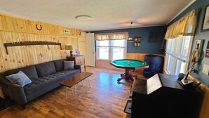 A room with a pool table, a sofa, a wooden wall with horse head decorations, and a window with blinds.