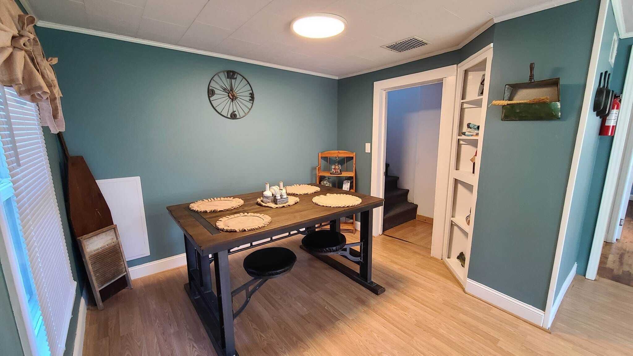 A dining area with a wooden table, four placemats, and a clock on the wall.