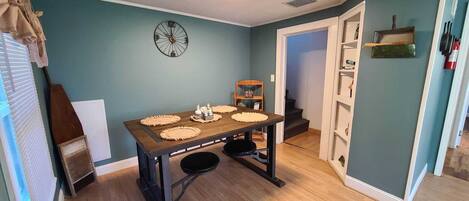 A dining area with a wooden table, four placemats, and a clock on the wall.