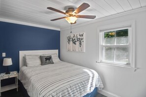 Une chambre à coucher avec un lit, un ventilateur de plafond, une table de chevet, une lampe et une fenêtre.