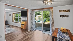 Un vaste espace de vie doté d’un plancher en bois, d’une porte-fenêtre coulissante donnant sur un jardin, et d’une table à manger agrémentée d’un chemin de table à motifs.