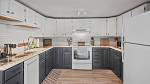 Une cuisine avec des armoires blanches, un plan de travail en bois, une cuisinière et un réfrigérateur.