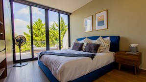 A bedroom with a large bed, a standing fan, a bedside table with a tissue box, and two framed pictures on the wall. - Capitalia Downtown Del Valle (Mexico City)
