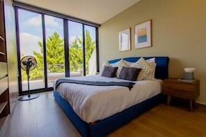 A bedroom with a large bed, a standing fan, a bedside table with a tissue box, and two framed pictures on the wall. - Capitalia Downtown Del Valle (Mexico City)