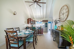 Un coin repas avec une table en bois dressée pour quatre personnes, un ventilateur de plafond et une horloge au mur.