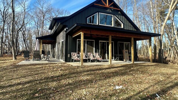 A modern house with a large porch, surrounded by trees.