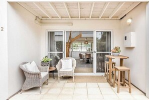 Relax in a spacious room with a sliding glass door to an outdoor area, a seating area with wicker chairs, and a casual dining space with a bowl of fresh fruit.
