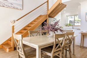 A dining area with a wooden table and chairs, a staircase, and a kitchen in the background.
